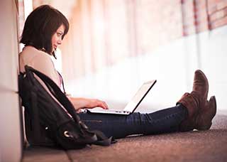 Image of a teen sitting on the ground, using a laptop